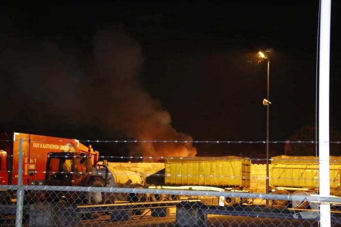 Grote berg afvalhout in brand naast houtopslag
