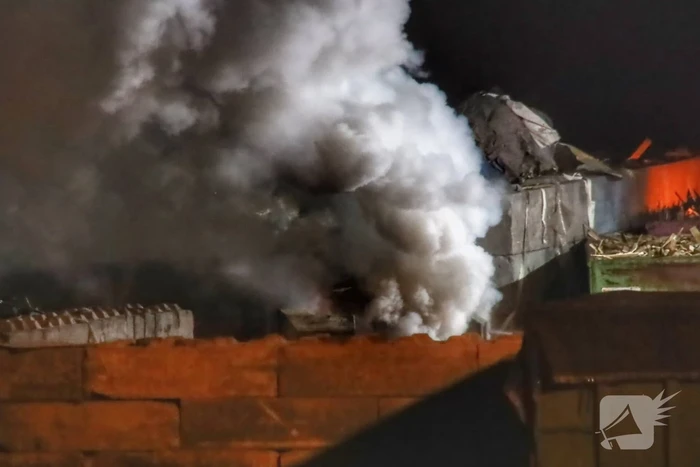 Grote berg afvalhout in brand naast houtopslag