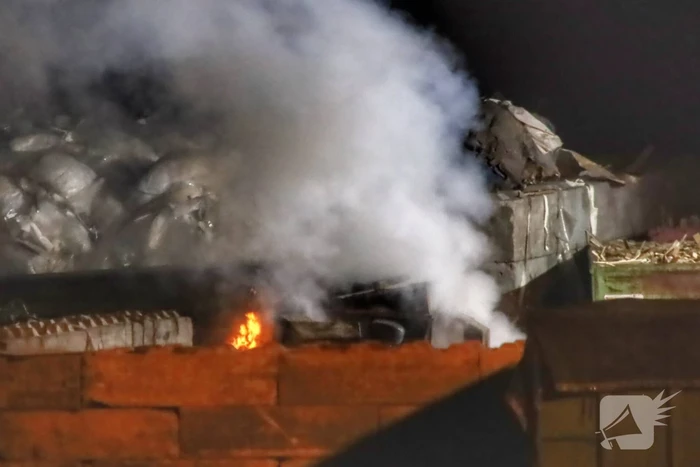 Grote berg afvalhout in brand naast houtopslag
