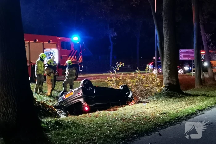 Personenauto ligt op zijn kop in berm