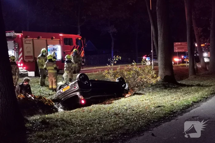 Personenauto ligt op zijn kop in berm