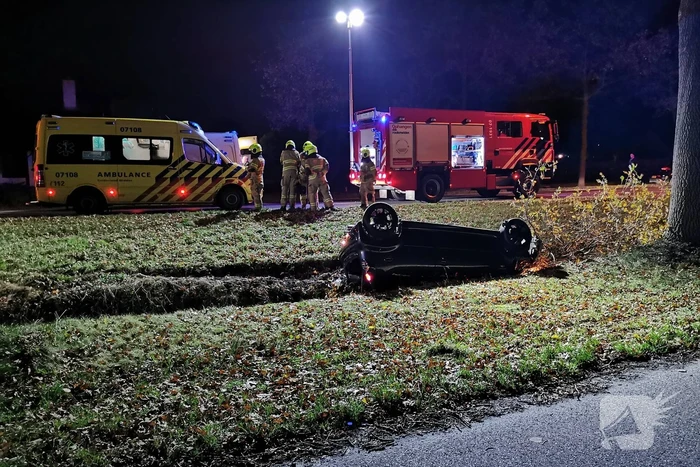 Personenauto ligt op zijn kop in berm