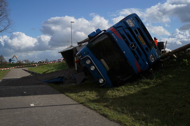 Vrachtwagen met zand van dijk gekanteld