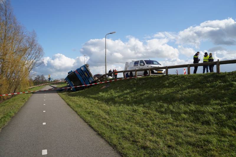 Vrachtwagen met zand van dijk gekanteld