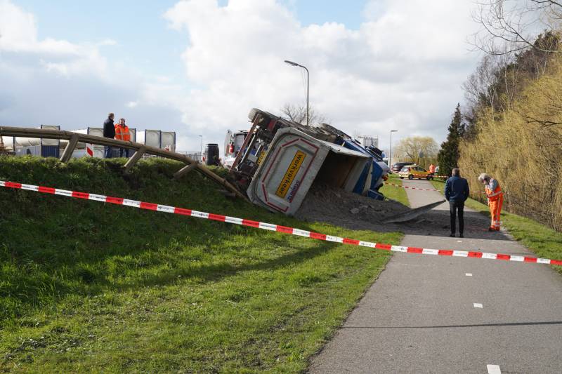 Vrachtwagen met zand van dijk gekanteld