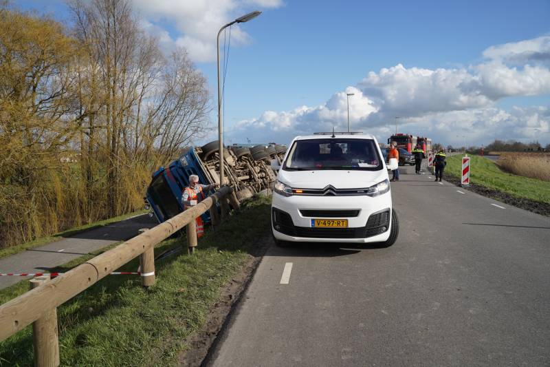 Vrachtwagen met zand van dijk gekanteld