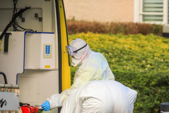 Mannen in witte pakken halen vermoedelijke coronapatiënt uit huis