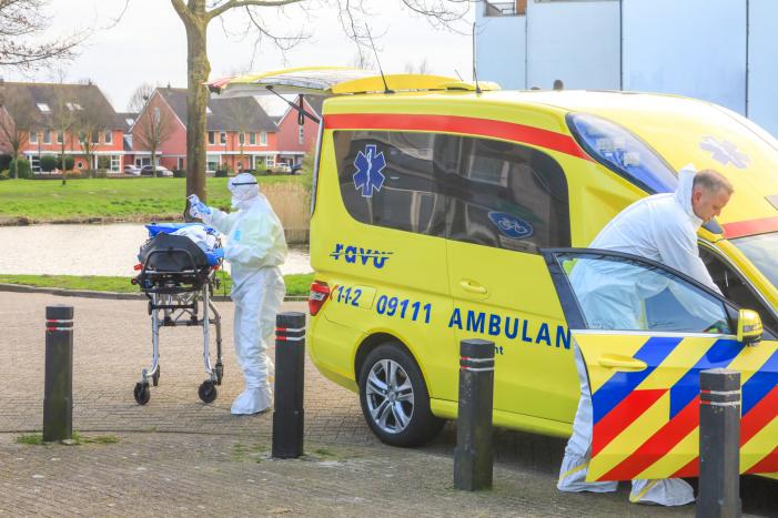 Mannen in witte pakken halen vermoedelijke coronapatiënt uit huis