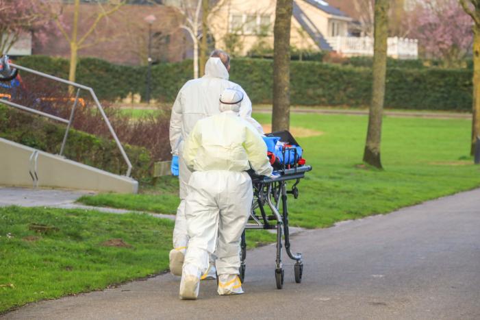 Mannen in witte pakken halen vermoedelijke coronapatiënt uit huis