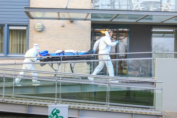 Mannen in witte pakken halen vermoedelijke coronapatiënt uit huis
