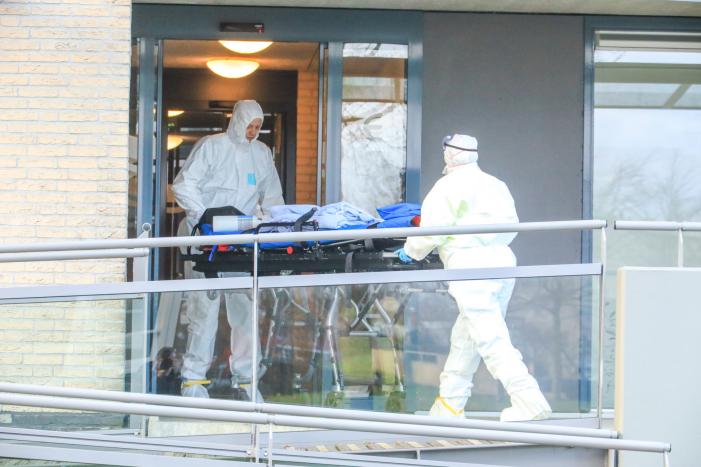 Mannen in witte pakken halen vermoedelijke coronapatiënt uit huis