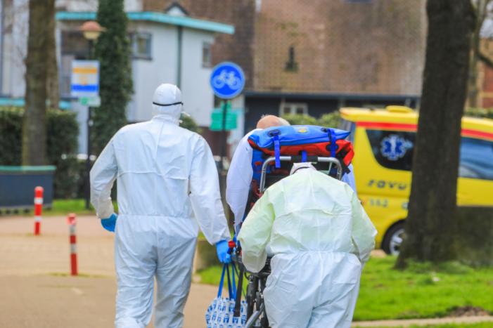 Mannen in witte pakken halen vermoedelijke coronapatiënt uit huis