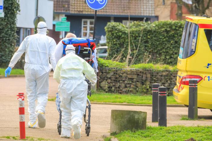 Mannen in witte pakken halen vermoedelijke coronapatiënt uit huis