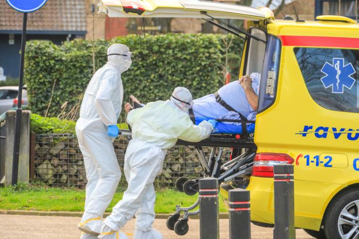 Mannen in witte pakken halen vermoedelijke coronapatiënt uit huis