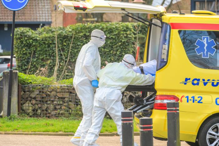 Mannen in witte pakken halen vermoedelijke coronapatiënt uit huis