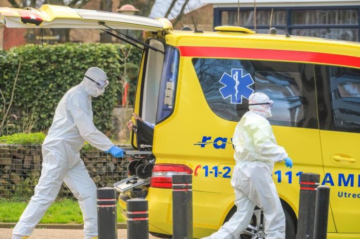 Mannen in witte pakken halen vermoedelijke coronapatiënt uit huis