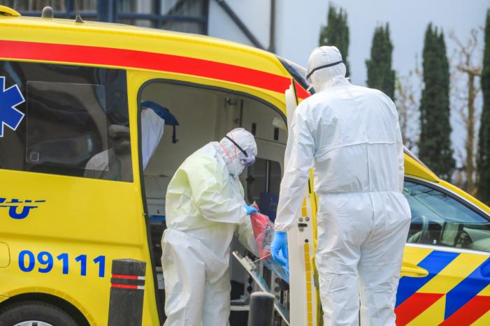 Mannen in witte pakken halen vermoedelijke coronapatiënt uit huis