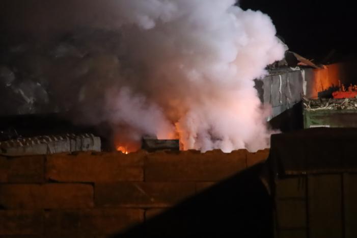 Grote berg afvalhout in brand naast houtopslag