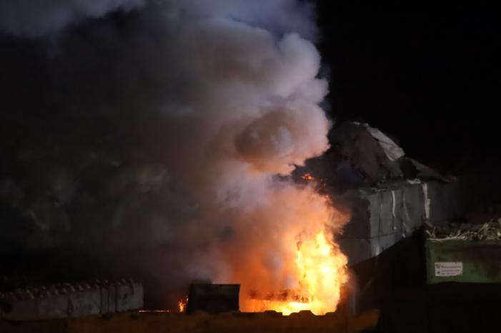 Grote berg afvalhout in brand naast houtopslag