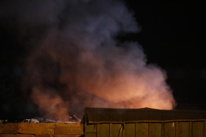 Grote berg afvalhout in brand naast houtopslag