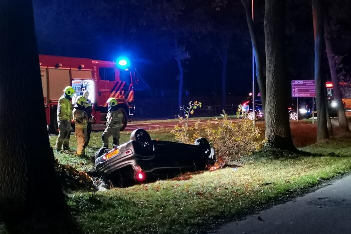 Personenauto ligt op zijn kop in berm