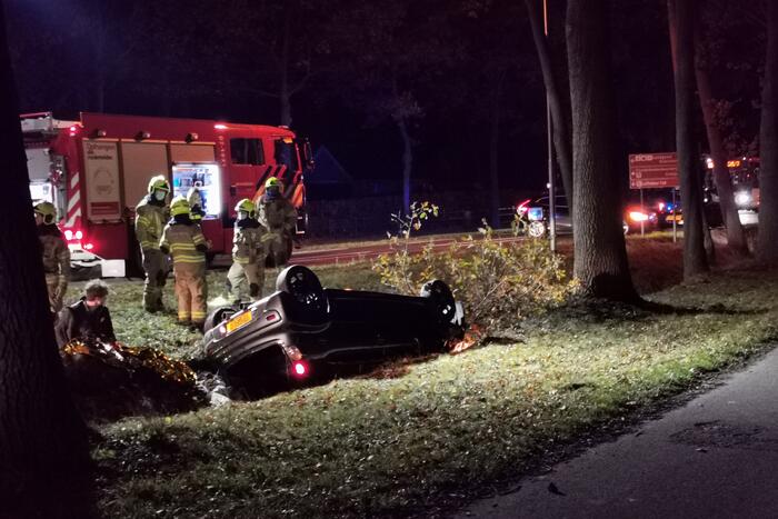 Personenauto ligt op zijn kop in berm