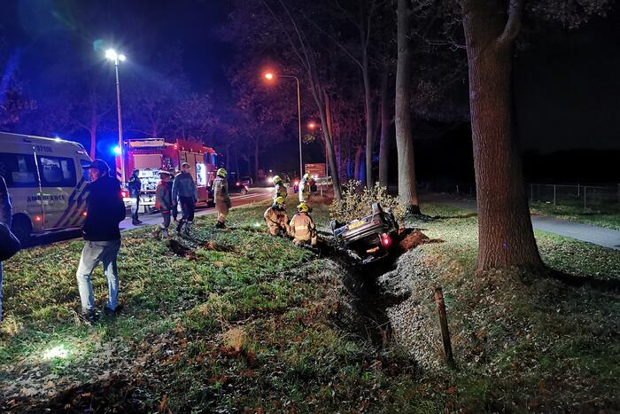 Personenauto ligt op zijn kop in berm