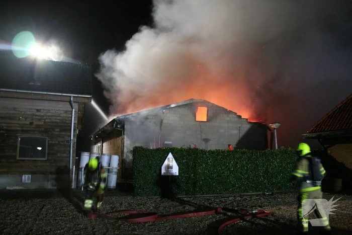 Grote uitslaande brand in loods achter woning