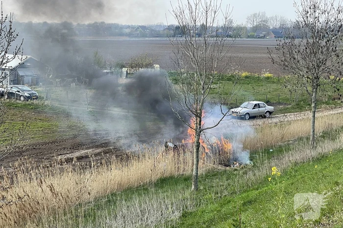 Auto glijdt van dijk af na botsing en vliegt in brand