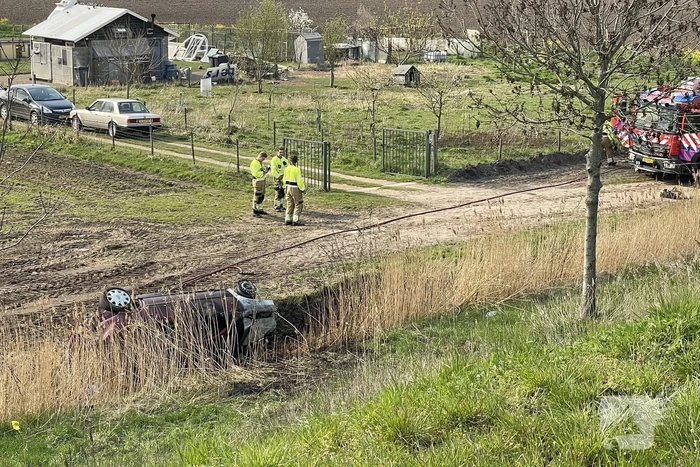 Auto glijdt van dijk af na botsing en vliegt in brand