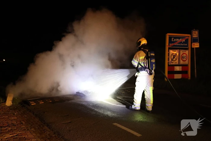Brandweer blust brandende band op midden van weg