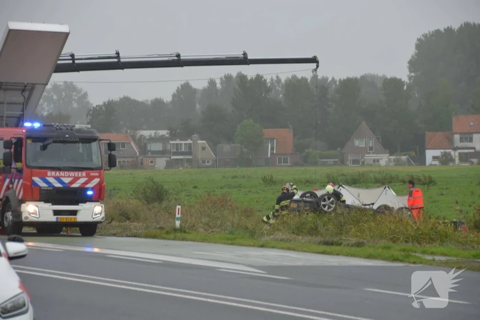 Auto raakt na botsing van de weg en belandt op de kop in weiland