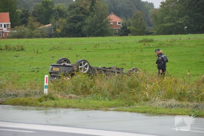 Auto raakt na botsing van de weg en belandt op de kop in weiland