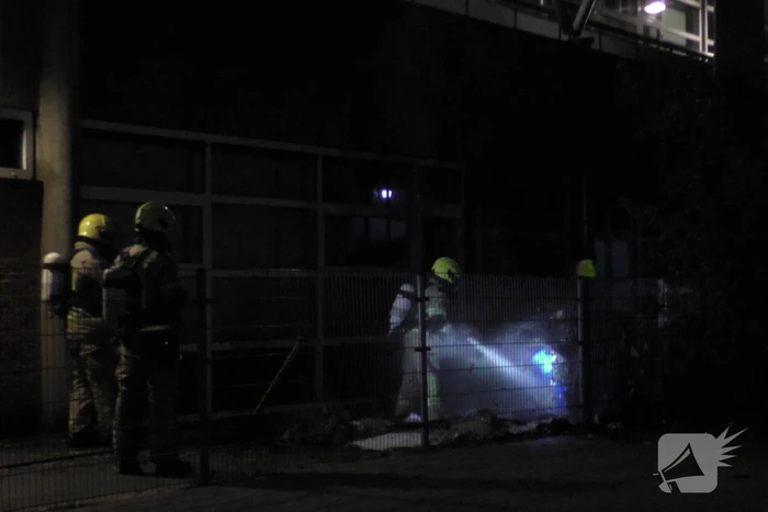 Brandweer blust brandende container tegen school