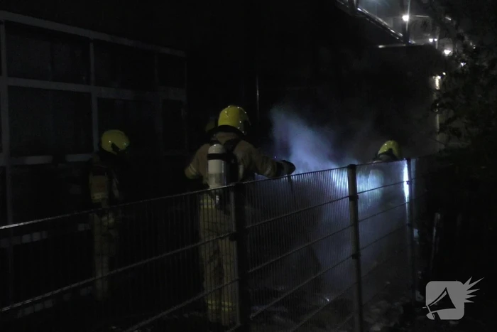 Brandweer blust brandende container tegen school