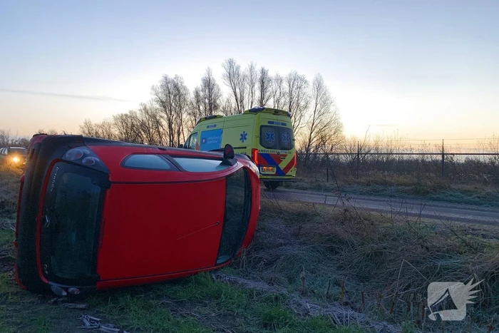Auto belandt op zijn kant langs spekgladde weg