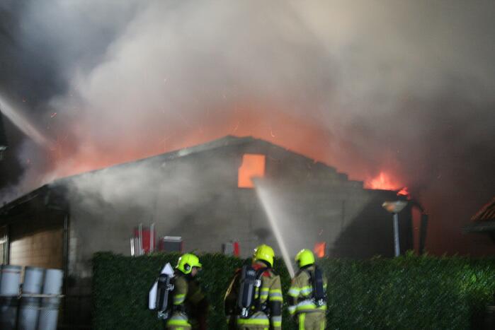 Grote uitslaande brand in loods achter woning