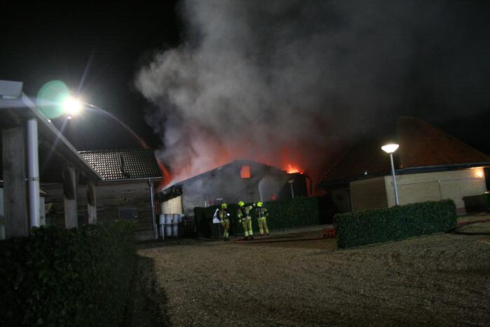 Grote uitslaande brand in loods achter woning