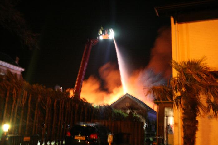 Grote uitslaande brand in loods achter woning