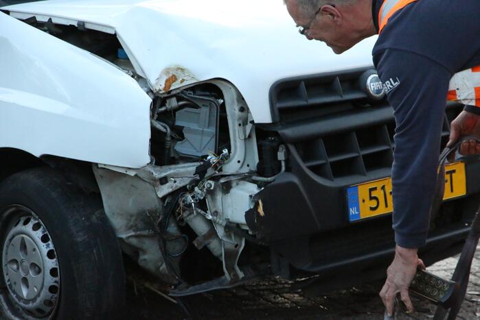 Busje op zijn kant na botsing met boom