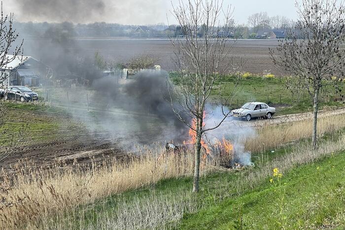 Auto glijdt van dijk af na botsing en vliegt in brand
