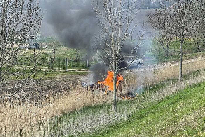 Auto glijdt van dijk af na botsing en vliegt in brand