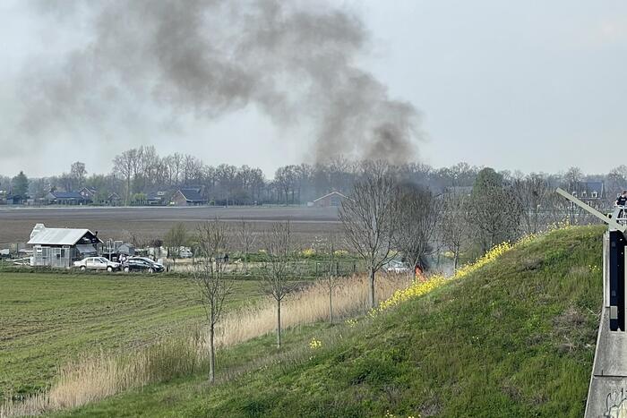 Auto glijdt van dijk af na botsing en vliegt in brand