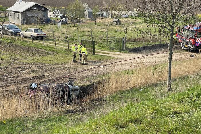 Auto glijdt van dijk af na botsing en vliegt in brand
