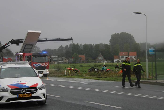 Auto raakt na botsing van de weg en belandt op de kop in weiland