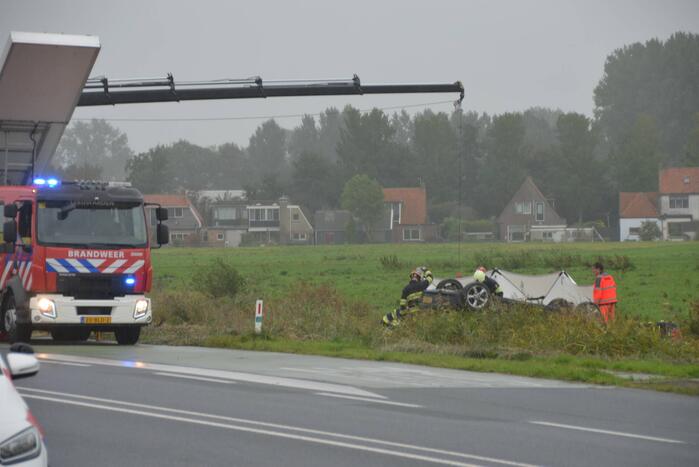 Auto raakt na botsing van de weg en belandt op de kop in weiland