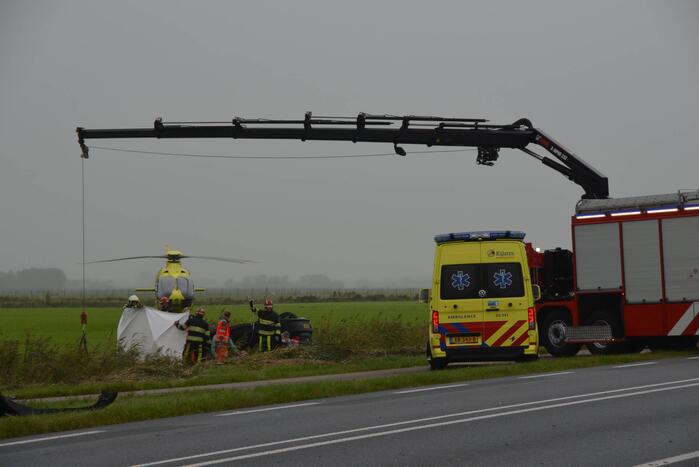 Auto raakt na botsing van de weg en belandt op de kop in weiland