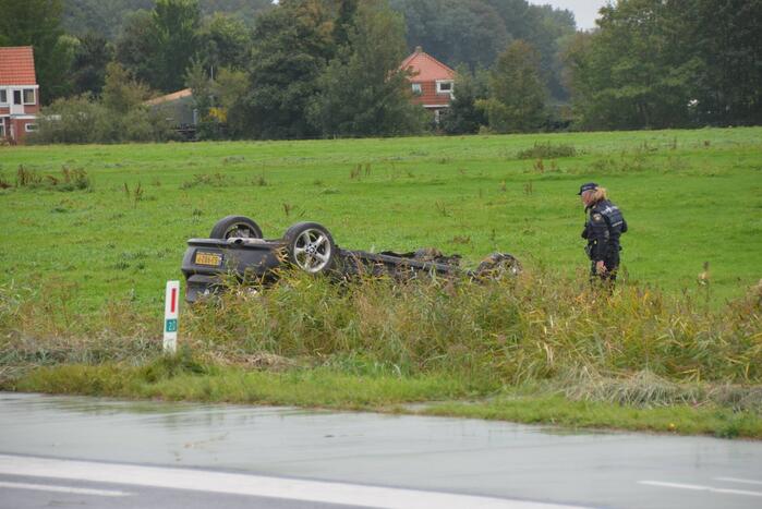 Auto raakt na botsing van de weg en belandt op de kop in weiland