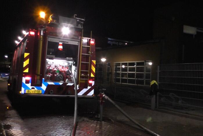 Brandweer blust brandende container tegen school