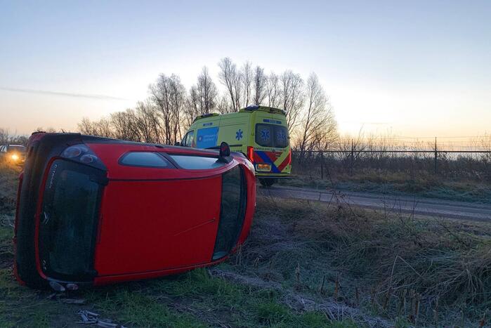 Auto belandt op zijn kant langs spekgladde weg